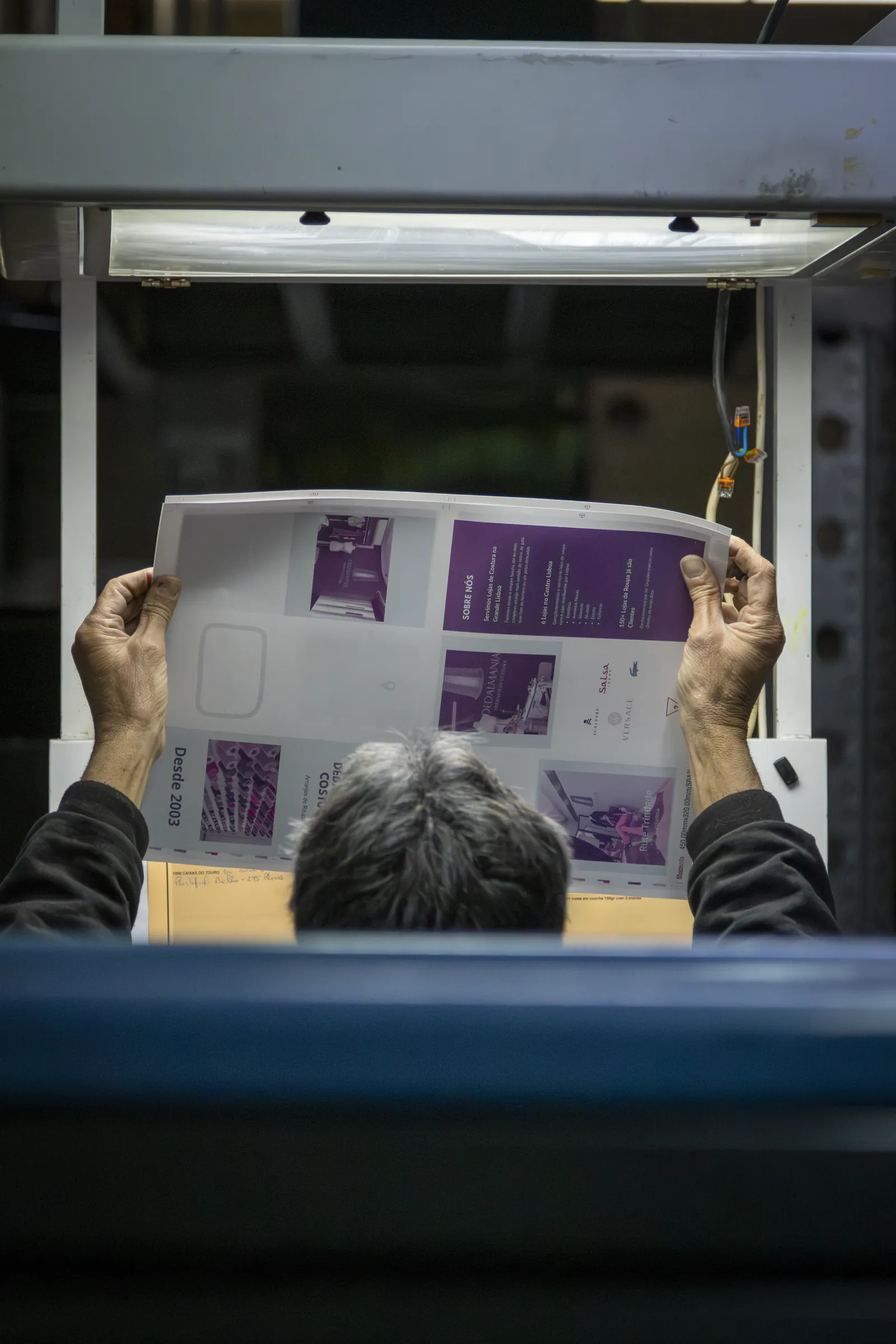 Uma folha de prova erguida contra a luz, à saída da máquina